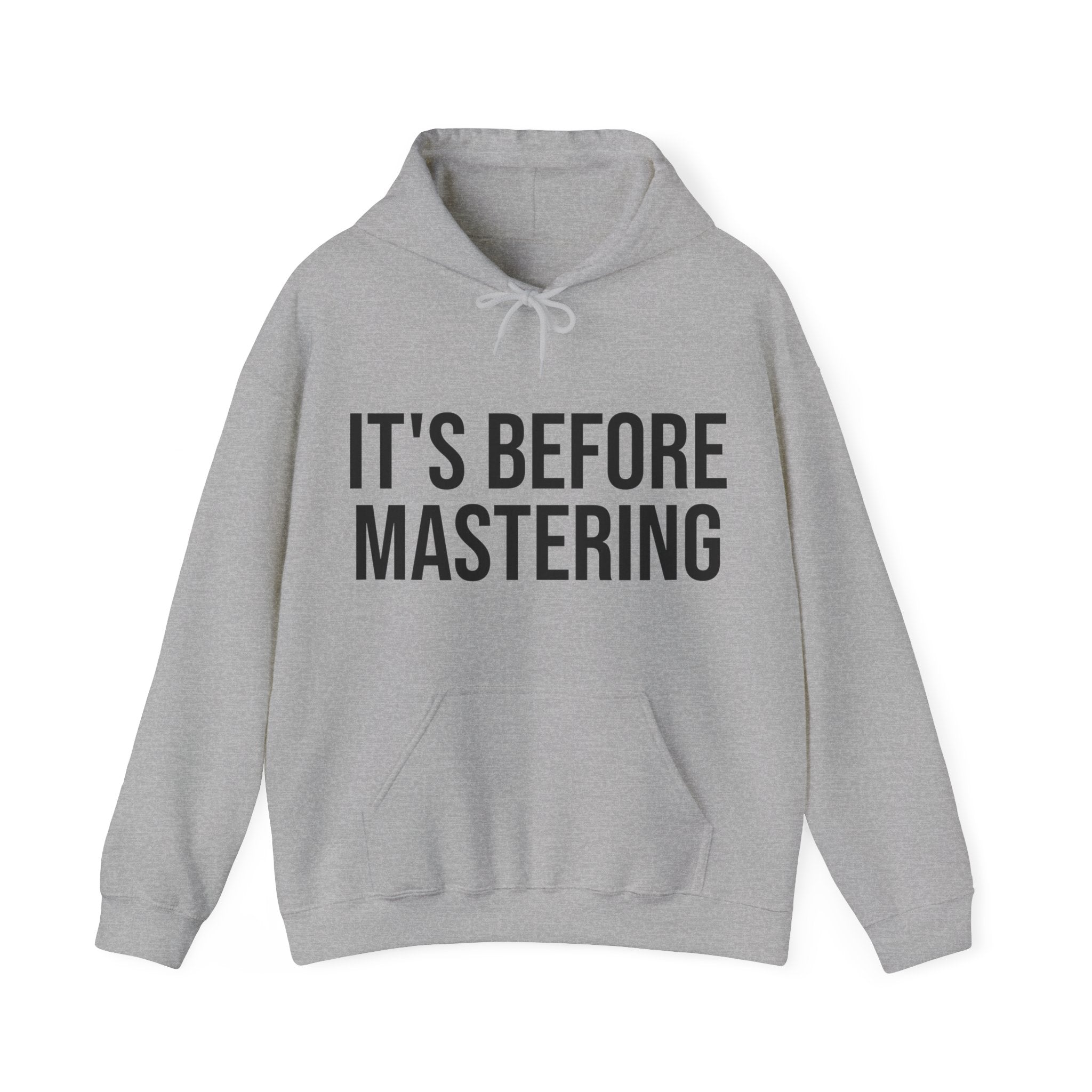 A heather grey hooded sweatshirt with a drawstring hood and a kangaroo pocket is laid out flat. Emblazoned across the chest in bold, block letters is the statement 'IT'S BEFORE MASTERING,' implying a stage in the audio production process before a track is fully produced. The typography and message resonate with music producers and audio engineers who appreciate the steps of music creation