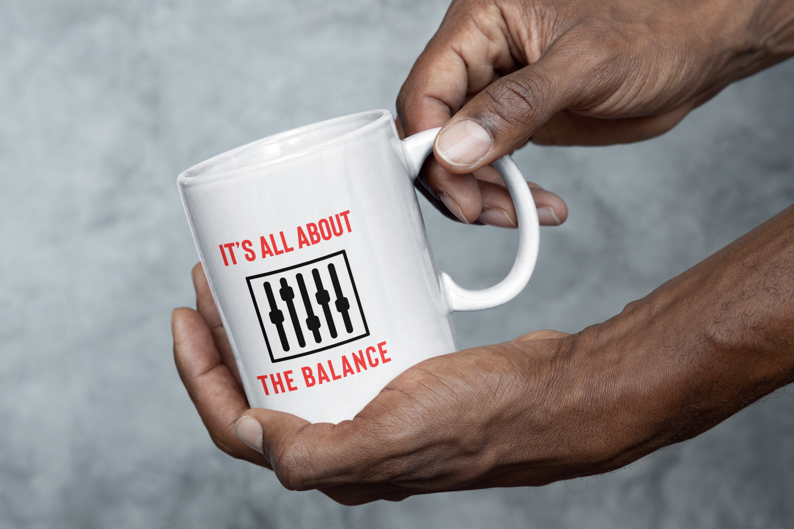 A hand holding a white mug with the phrase "IT'S ALL ABOUT THE BALANCE" and a graphic of audio mixing sliders, symbolizing the meticulous craft of balancing sounds in music production.